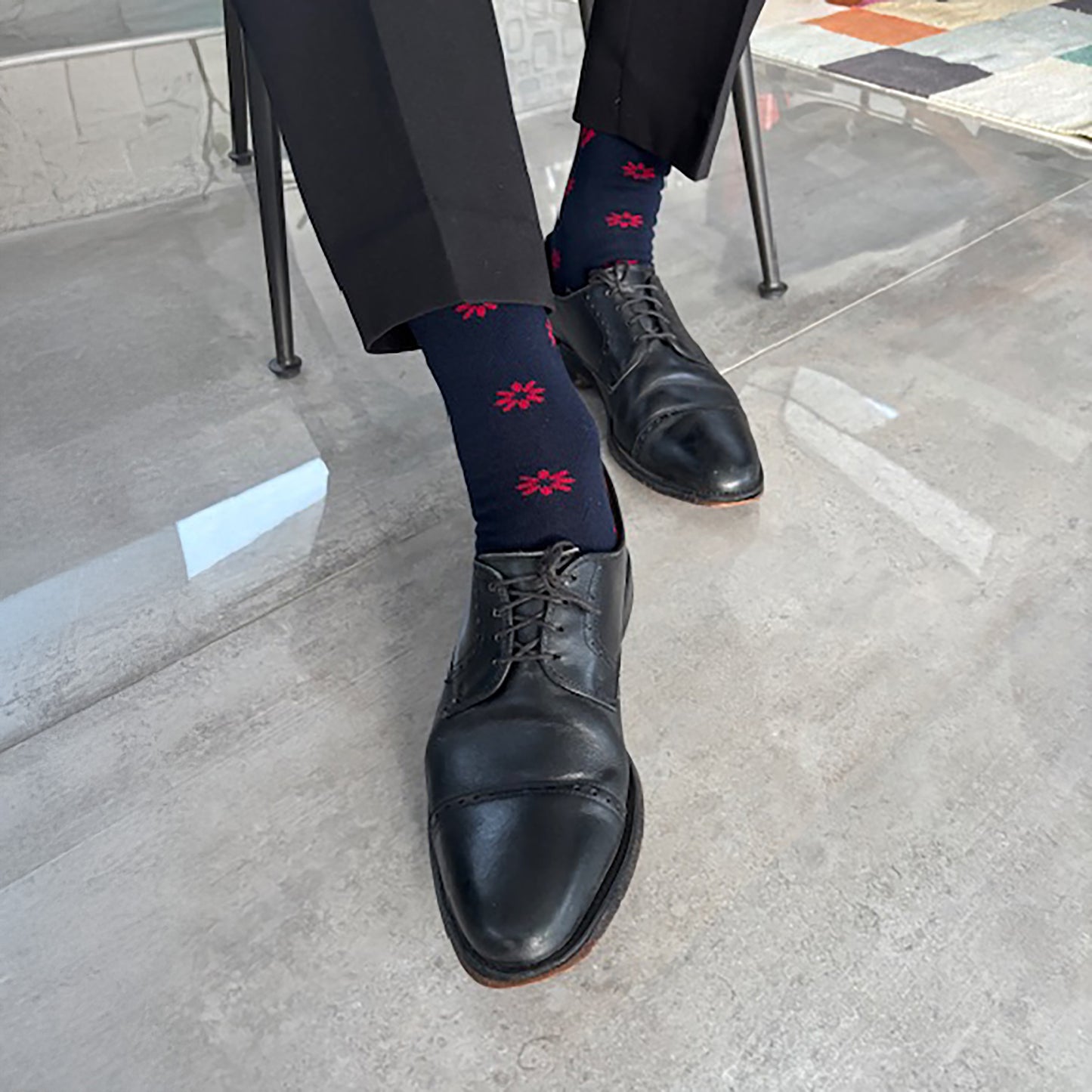 A person wearing navy dress shoes and dark blue socks with red patterns on a concrete floor.